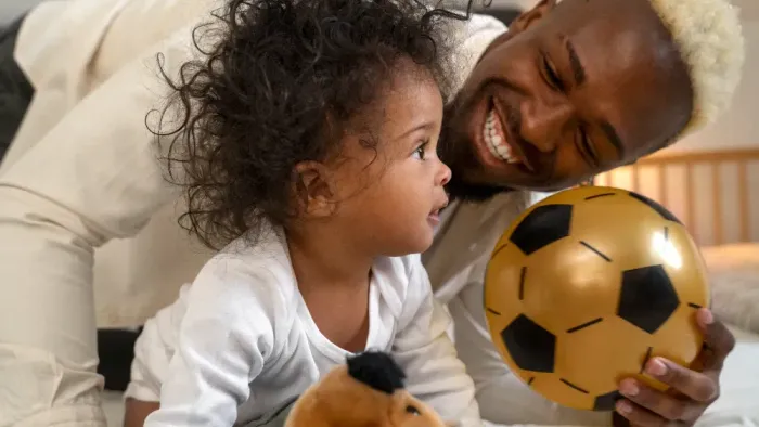 Ein Kind und ein Erwachsener spielen mit einem Fußball auf einem Bett.