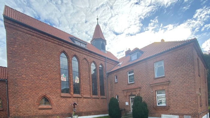 Ein rotes Backsteingebäude mit spitzem Turm und bogenförmigen Fenstern unter einem bewölkten Himmel.
