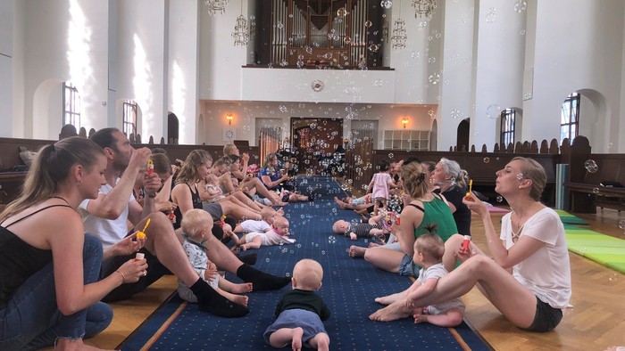En gruppe kvinder og børn deltager i en yoga- eller dansestund i en kirke.