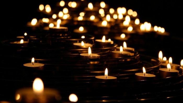 Numerous lit candles arranged in a dark setting, creating a warm and serene atmosphere.