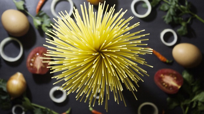 Billede af gule nudler, tomater, æg og grønne urter på sort baggrund