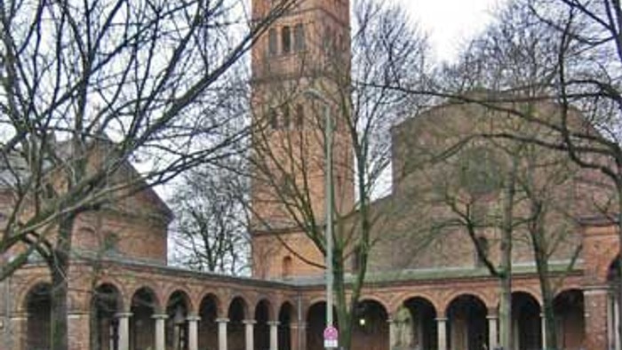 Ein rotes Auto fährt vor einer großen Ziegelkirche mit hohem Turm.