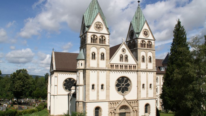 Ein großes, weißes Kirchengebäude mit zwei grünen Türmen und einem großen Uhrwerk im Vordergrund.