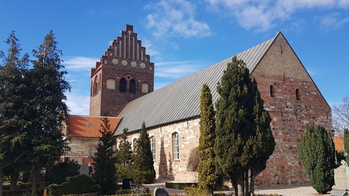 Historisk murstenskirke med et højt tårn og traditionelt arkitektonisk design i et anlagt område.