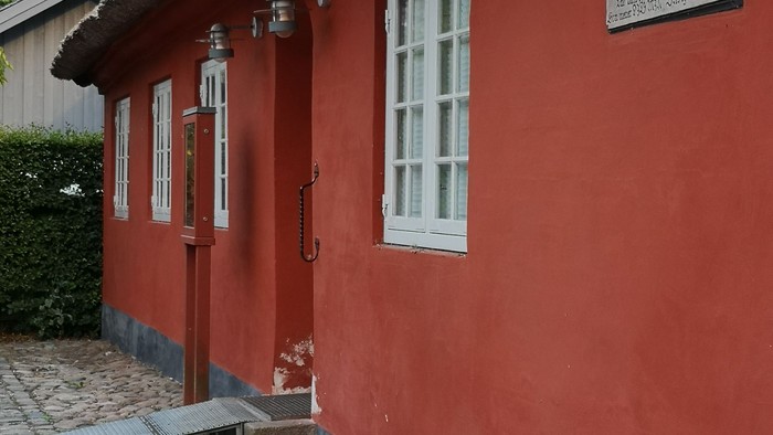 Rødt hus med hvide vinduer og skilt på væggen