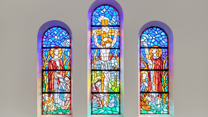 Tre farverige glasvinduer med religiøse motiv i bueform