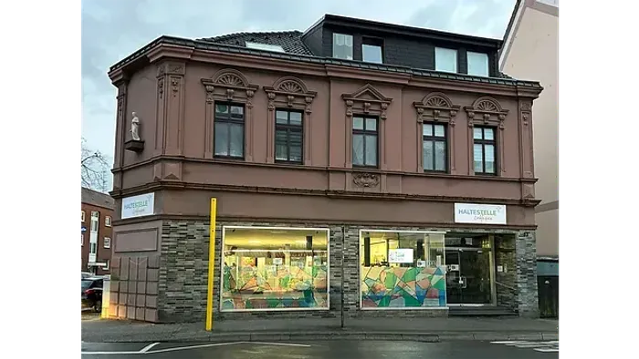 Zweigeschossiges Gebäude mit Ladengeschäften, davon eines leerstehend, an einer Straßenecke.