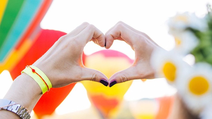 Zwei Hände bilden ein Herz vor bunten Luftballons