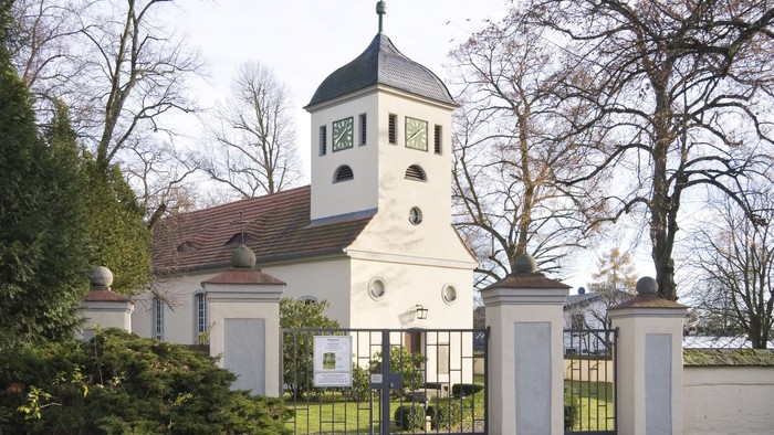 Weißes Gebäude mit Uhrturm und schwarzem Dach hinter hohem Tor