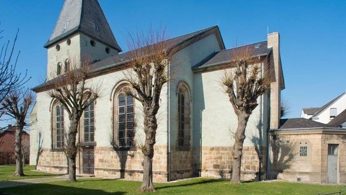 Ein weißer Kirchenbau mit spitzem Turm und großen Fenstern vor blauem Himmel.