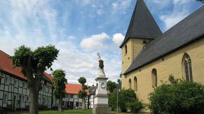 Ein Kirchenhof mit einem Denkmal und einem Kirchturm unter blauem Himmel