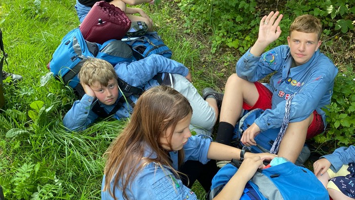 En gruppe unge på ture, sidder på græs med rygskuder og teltudstyr.