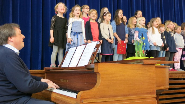 Ein Mann spielt Klavier, während ein Kinderchor singt