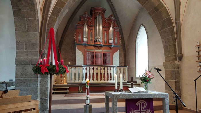 Blick auf die Orgel in der Evangelischen Kirche Ahnatal-Weimar, im Vordergrund eine Truhenorgel, ein Adventskranz, Kerzen und der Altar