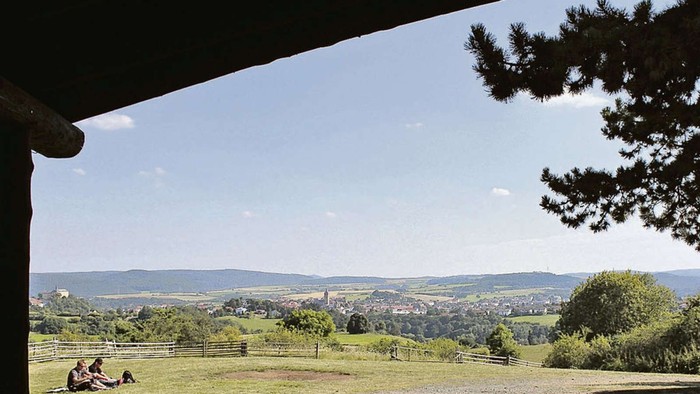 Die Menschen entspannen sich an einem Hang mit Blick auf eine malerische, ländliche Landschaft unter einem klaren Himmel.
