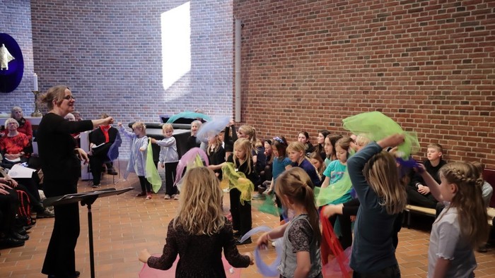 En gruppe børn og voksne deltager i en aktivitet i et rum med mur af røde mursten.