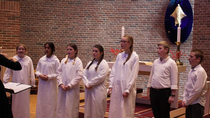 En gruppe unge piger og en dreng i hvide tøjer står i en kirke.