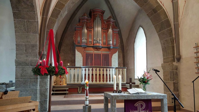 Blick auf die Orgel in der Evangelischen Kirche Ahnatal-Weimar, im Vordergrund eine Truhenorgel, ein Adventskranz, Kerzen und der Altar