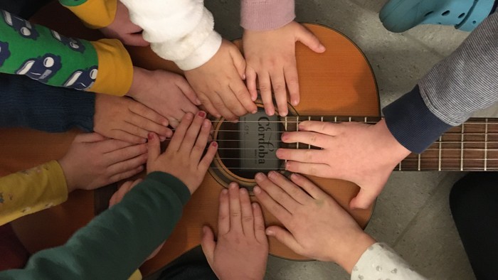 Kinder bilden einen Kreis und legen ihre Hände auf eine Gitarre