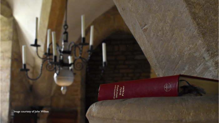 A red book rests on a stone ledge beneath a chandelier in a rustic room.