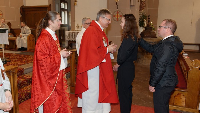Eine Gruppe von Menschen in einer Kirche, einige in roten und weißen Gewändern, andere in formeller Kleidung.