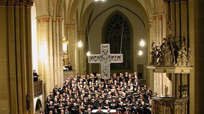Große Menschenmenge in einer Kirche, viele sitzen, einige stehen, große Kreuz an der Wand