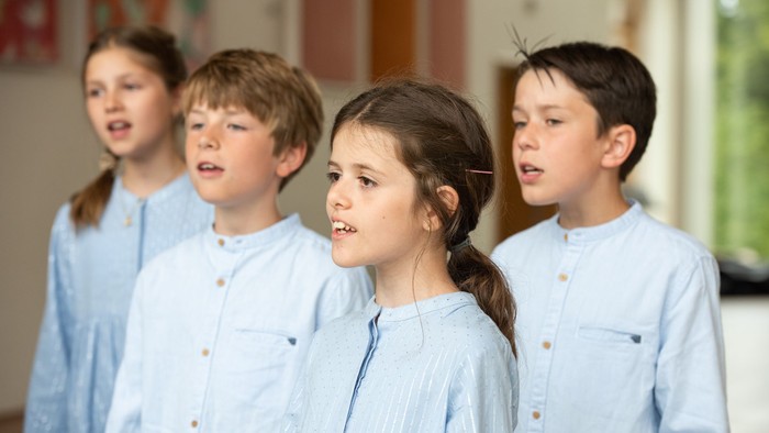 Fire børn står i en linje og synger. De er alle i blå klæder.