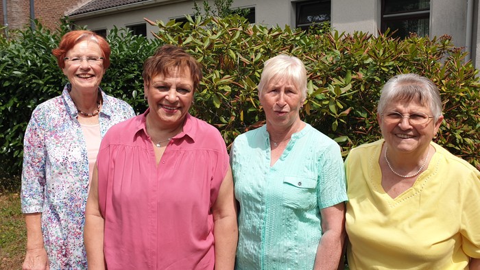 Vier ältere Frauen stehen vor einem Haus und lächeln