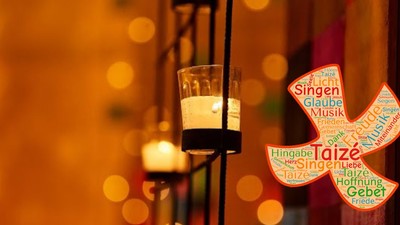 Dekorative Taizé-Gebetslaterne mit bunten Worten und einer brennenden Kerze vor unscharfem Hintergrundlicht.