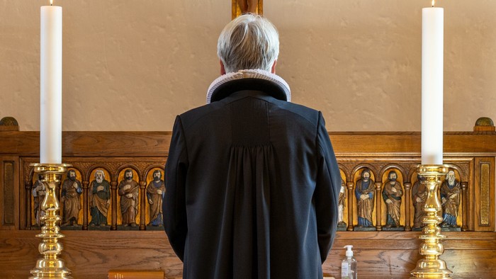 En præst står i en kirke og ser op mod alteret med lysede steariner.
