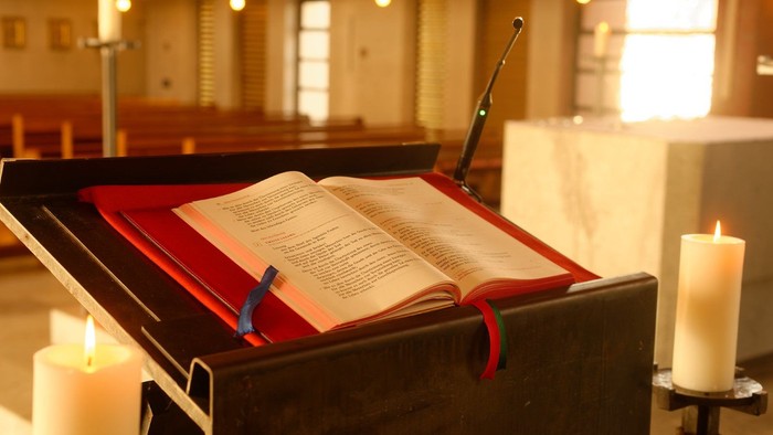 Offene Bibel auf Lesepult in Kirche mit brennenden Kerzen