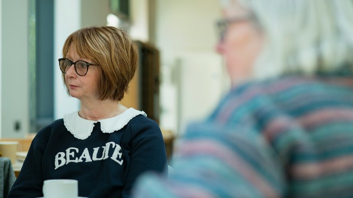 Eine Frau mit Brille sitzt an einem Tisch und trinkt Tee.