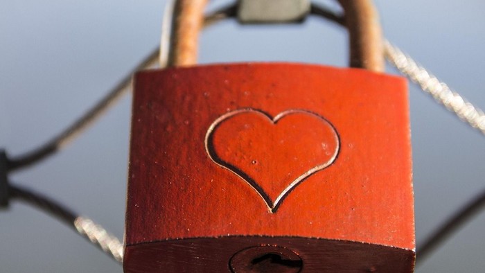 Rød hængelås med hjerteform fastgjort til et trådhegn.