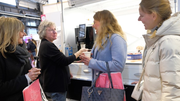 Eine Gruppe von Menschen, die in einem Café interagieren, wobei eine Person einer anderen eine Tasse reicht.