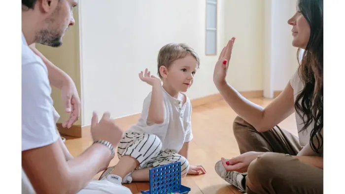 Eltern spielen mit dem Baby auf dem Boden und heben alle die Hände.