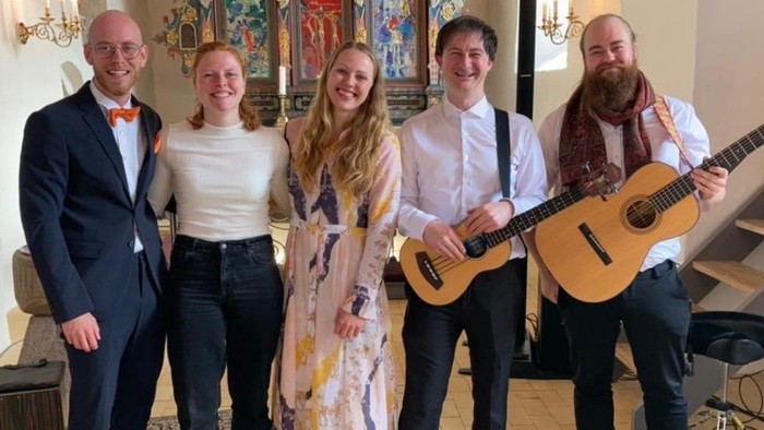 En gruppe af fem personer poser med guitarer i en kirke