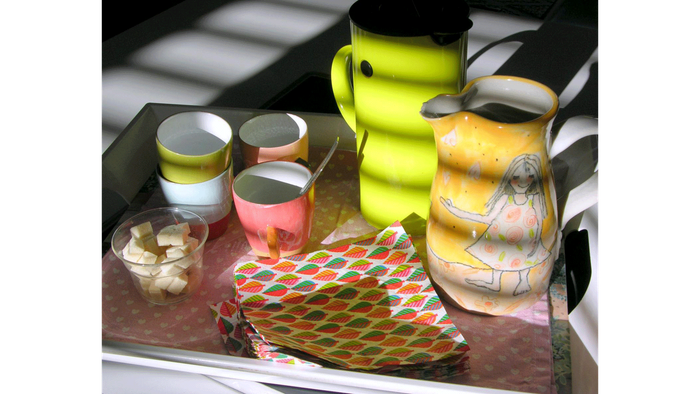 Bunte Vintage-Teekanne, Tassen und gemustertes Tablett mit Snacks auf einer rustikalen Metalloberfläche.