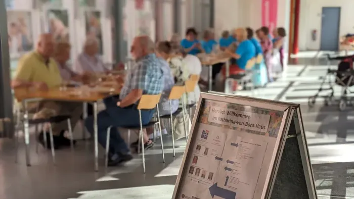 Menschen, die an Tischen in einem öffentlichen Bereich sitzen, mit einem Schild im Vordergrund.