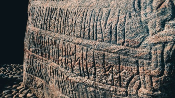 Gammel sten cylinder med indviklede kileskriftudskæringer og slidte overfladedetaljer.