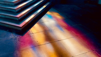 Lebendige Lichtstreifen erzeugen eine farbenfrohe Reflexion auf einem dunklen, gefliesten Boden unter einer Treppe.