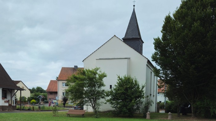 Im Vordergrund eine große steinerne Vogeltränke, im Hintergrund eine weiße Kirche mit hohem Turm und umgebende Häuser.