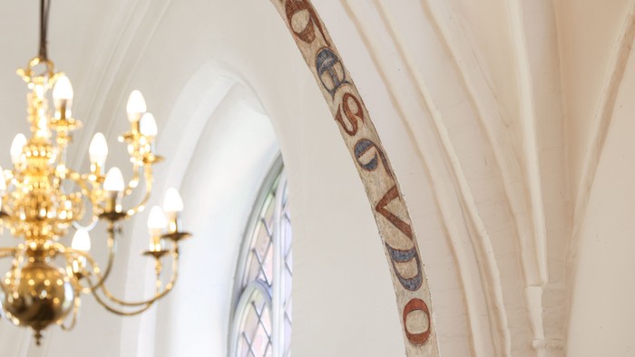 En belysning hænger fra loftet i en kirke med et bogstaveligt maleri på væggen.