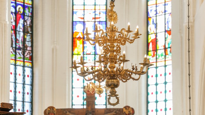Et elegant, prægtigt lysekrone hænger over et farvet glasmosaikvindue i en kirkes indre.