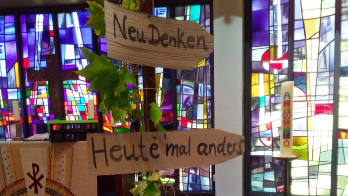 Kreative Holzschilder auf einem Ständer, die verschiedene Denkansätze in einem farbenfrohen Kirchenfenster-Raum bewerben.