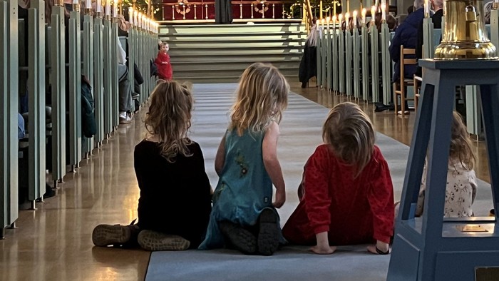 Tre børn sidder i en kirke.