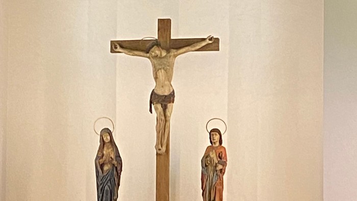 Religiöse Altarszene mit einer Kreuzigungsstatue, Figuren von Maria und Johannes sowie umgebenden Gläubigen.