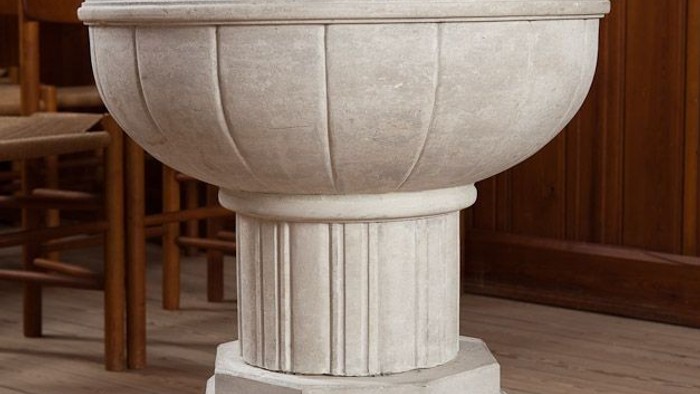 Elegant sten dåbsfad med indviklede udskæringer og en sokkelbase i en kirkelig indstilling.