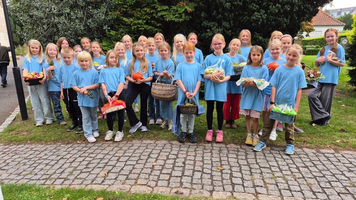 Brønshøj Kirkes Børnekor står foran kirken med gavekurve til høstauktion i armene.