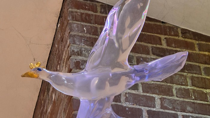 En gennemskinnelig glaskulptur af en fugl i flugt, der hviler på en murstensafsats.