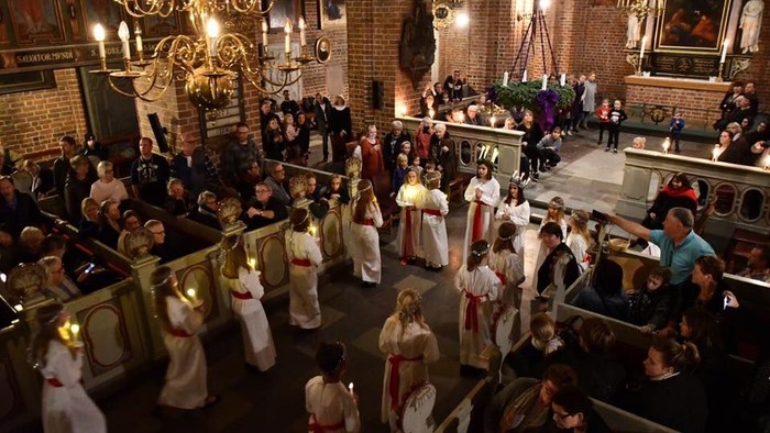 Religiøs procession inde i en kirke med deltagere, der bærer lys og tændte fakler under en ceremoni.